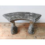 A WEATHERED CURVED SEATED RECONSTITUTED STONE GARDEN BENCH, the two supports with carved fish