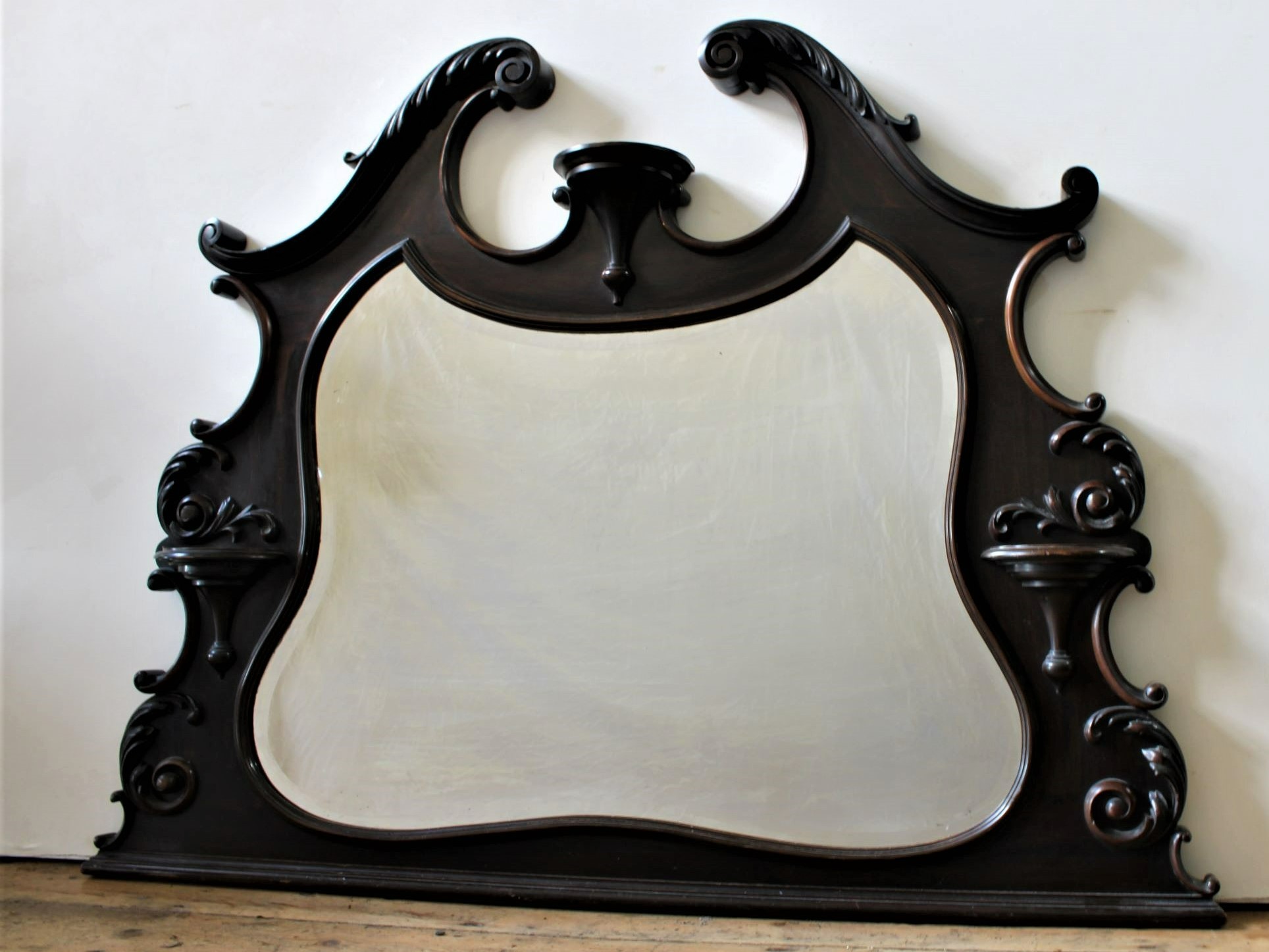 AN ORNATE CARVED FRAMED OVERMANTEL MIRROR, the bevelled mirror contained within an ornate scroll