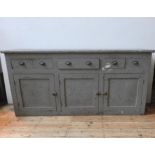 A RUSTIC DISTESSED PAINTED THREE DOOR PINE DRESSER BASE, with three drawers fitted with brass cup