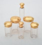 A set of six facetted glass dressing table jars with gilded caps