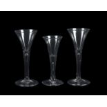 A group of three plain stemmed wine glasses of drawn trumpet form