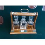 An Edwardian oak and EPNS banded 3 bottle tantalus with original bottles and sterling silver