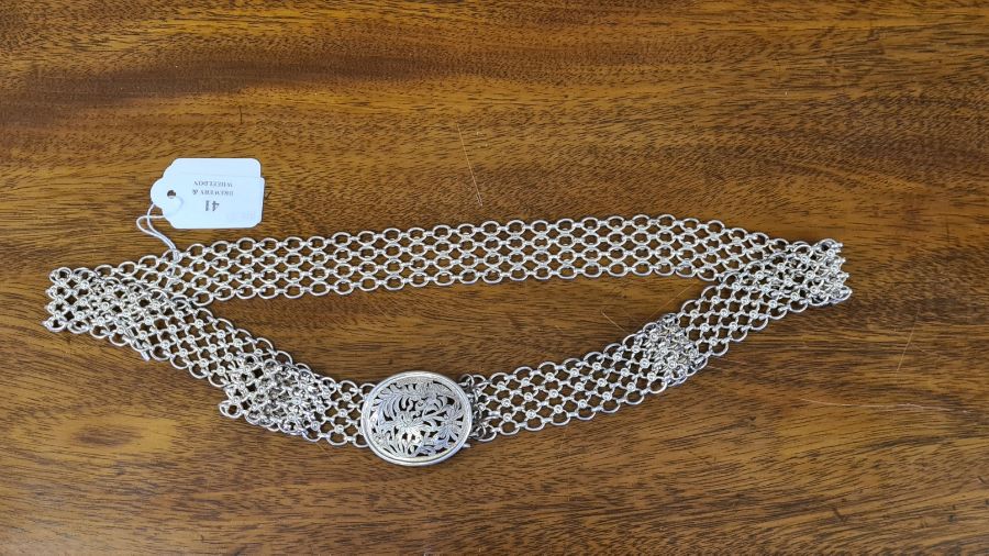 An Asian silver chain belt and cast buckle with pierced oval face 184g.