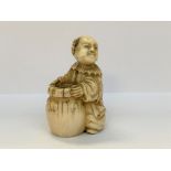 NETSUKE en ivoire figurant Karako souriant se tenant près d'une jarre (gerce rebouchée). Japon,