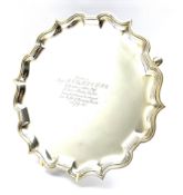 Silver circular salver with pie crust border, presentation inscription and on triple shaped supports