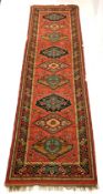 Red ground woollen runner rug, with lozenge and geometric design enclosed by multi line border, 340c