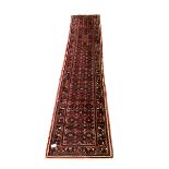 Central Asian runner rug, with repeating lozenge motif on busy red field, stylised foliate to border