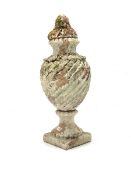 Lidded terracotta urn, the wrythen body supported by a socle on square base, well weathered and with