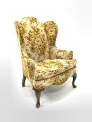 20th century wing back armchair, upholstered in floral fabric with squab cushion, raised on cabriole