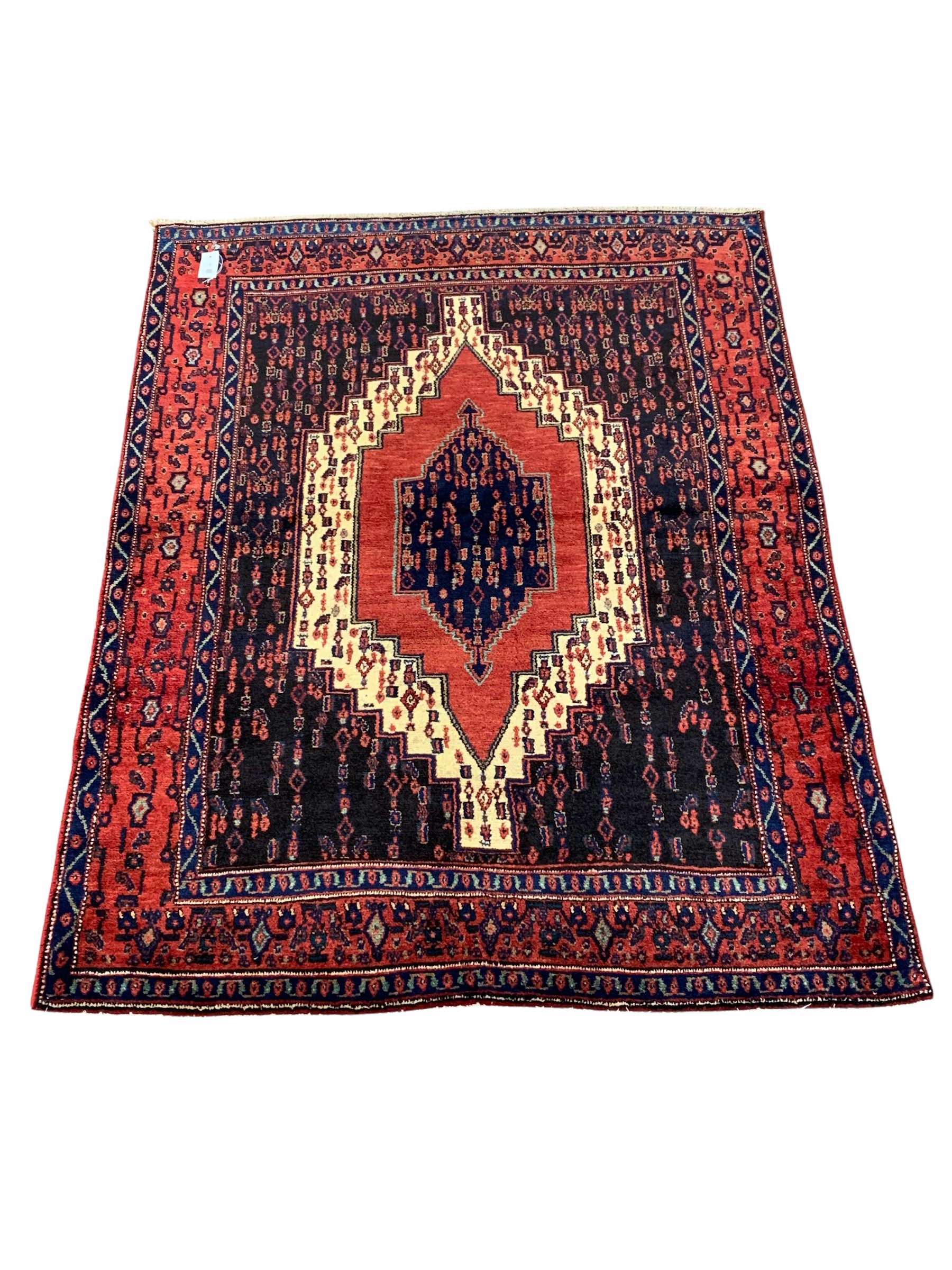 Persian senneh hand knotted red ground rug centred by a geometric medallion and bordered 165cm x 120