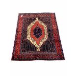 Persian senneh hand knotted red ground rug centred by a geometric medallion and bordered 165cm x 120