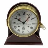Eight-day 20th century brass cased ships bulkhead clock mounted on a mahogany effect display stand