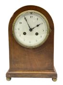 An Edwardian mantle clock in an arched mahogany case inlaid with satinwood stringing on a moulded pl