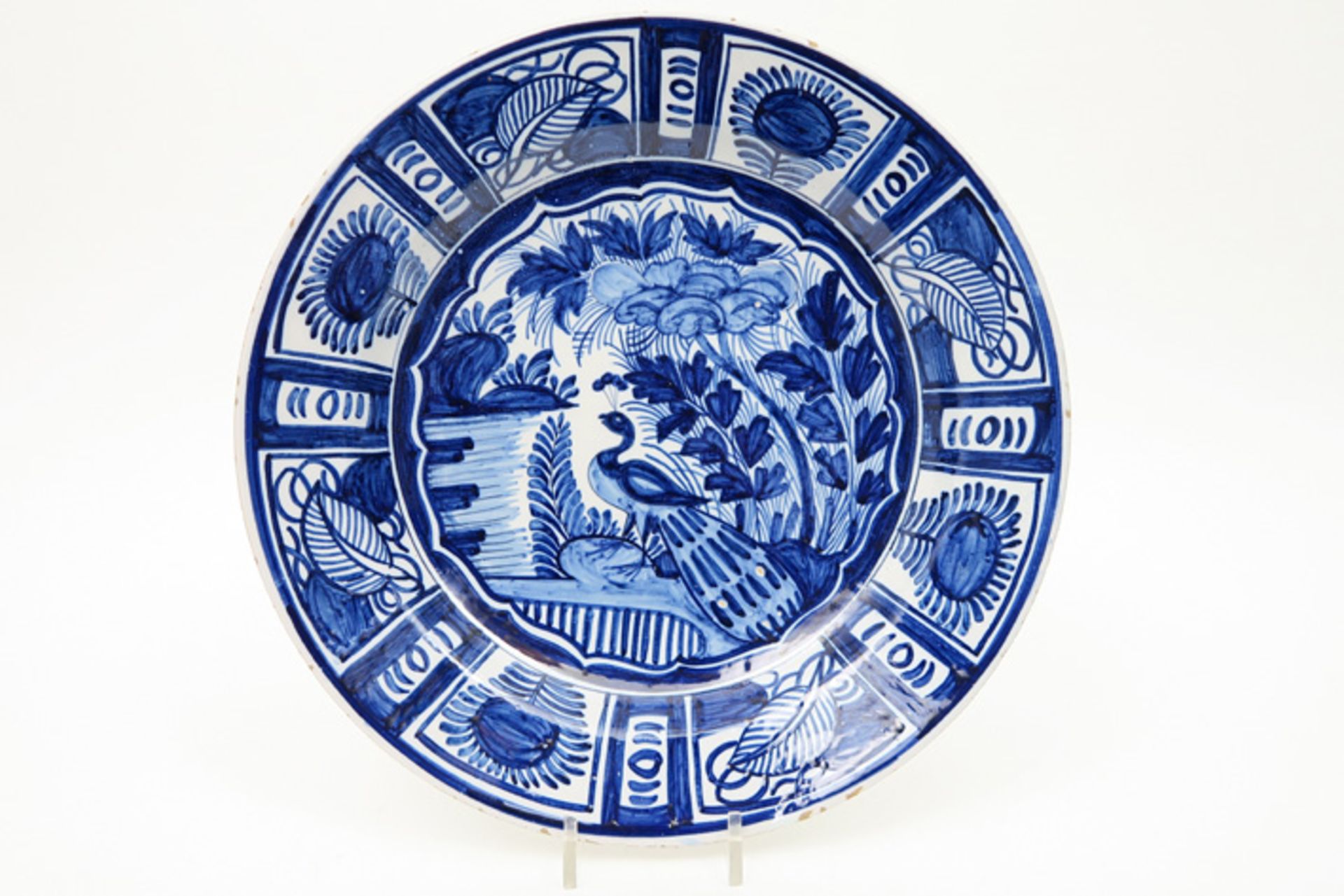 quite big 18th Cent. dish in ceramic from Delft with a blue-white peacock in garden decor Achttiende