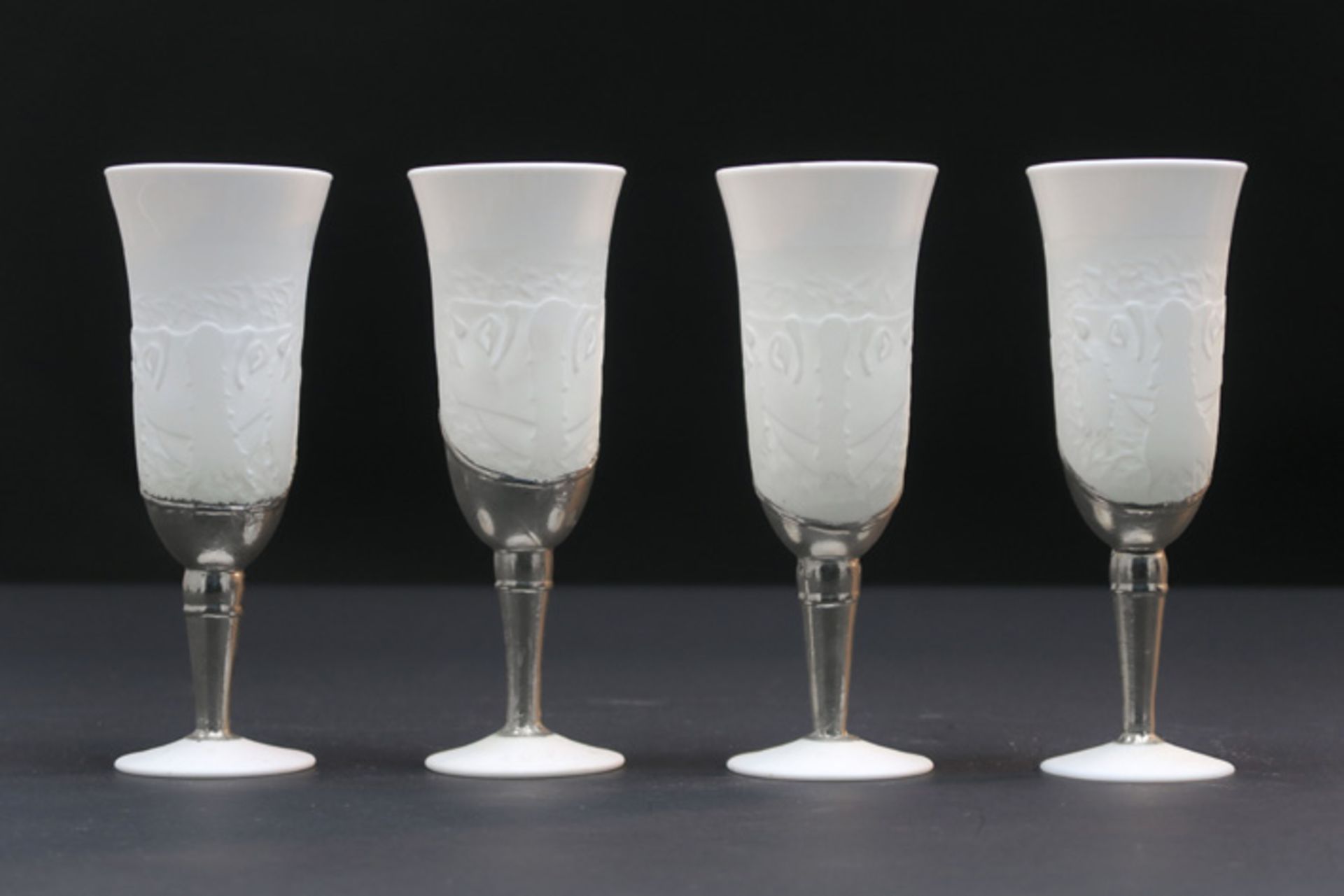 LEIBOVITZ EDWARD (1946 - 2019) serie van vier champagneglazen in wit opaak glas met een metalen