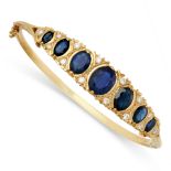 A SAPPHIRE AND DIAMOND BANGLE in 9ct yellow gold, the hinged body set to one half with a row of