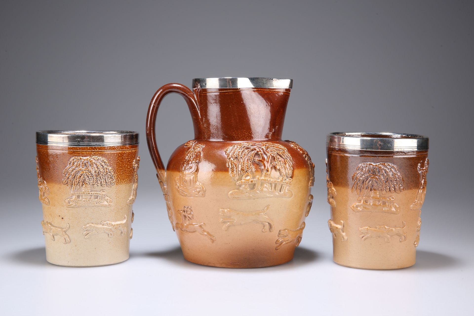 A VICTORIAN SILVER-RIMMED SALT-GLAZED STONEWARE PITCHER AND PAIR OF BEAKER CUPS