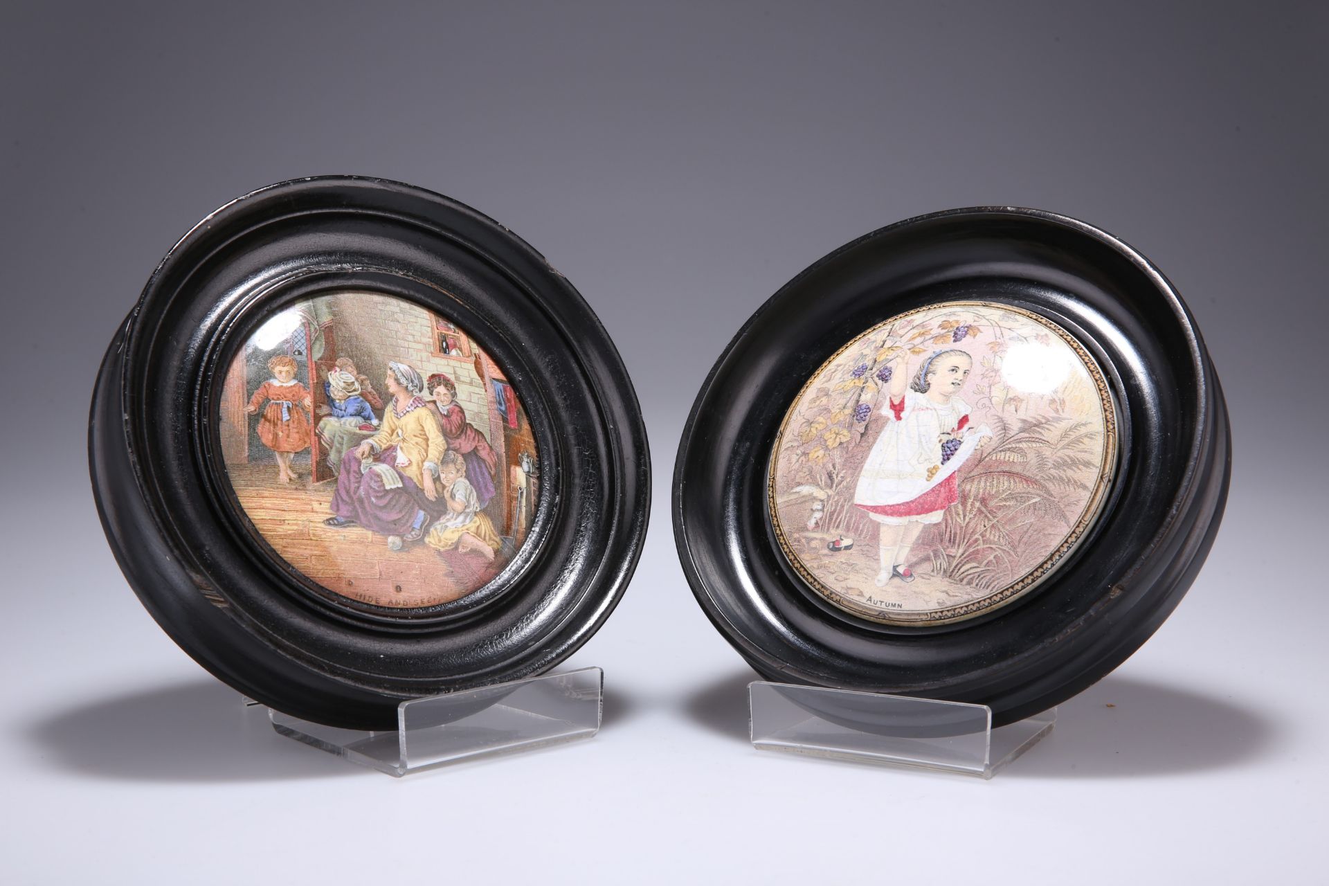 A PAIR OF VICTORIAN POT LIDS, "HIDE AND SEEK" AND "AUTUMN", in moulded circular frames. 16.5cm