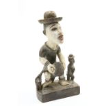 A carved and painted tribal figure group, the standing figure with brass hat, 57cm high