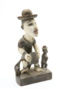 A carved and painted tribal figure group, the standing figure with brass hat, 57cm high