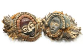 Two carved tribal masks, each applied with shells and feathers