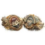 Two carved tribal masks, each applied with shells and feathers