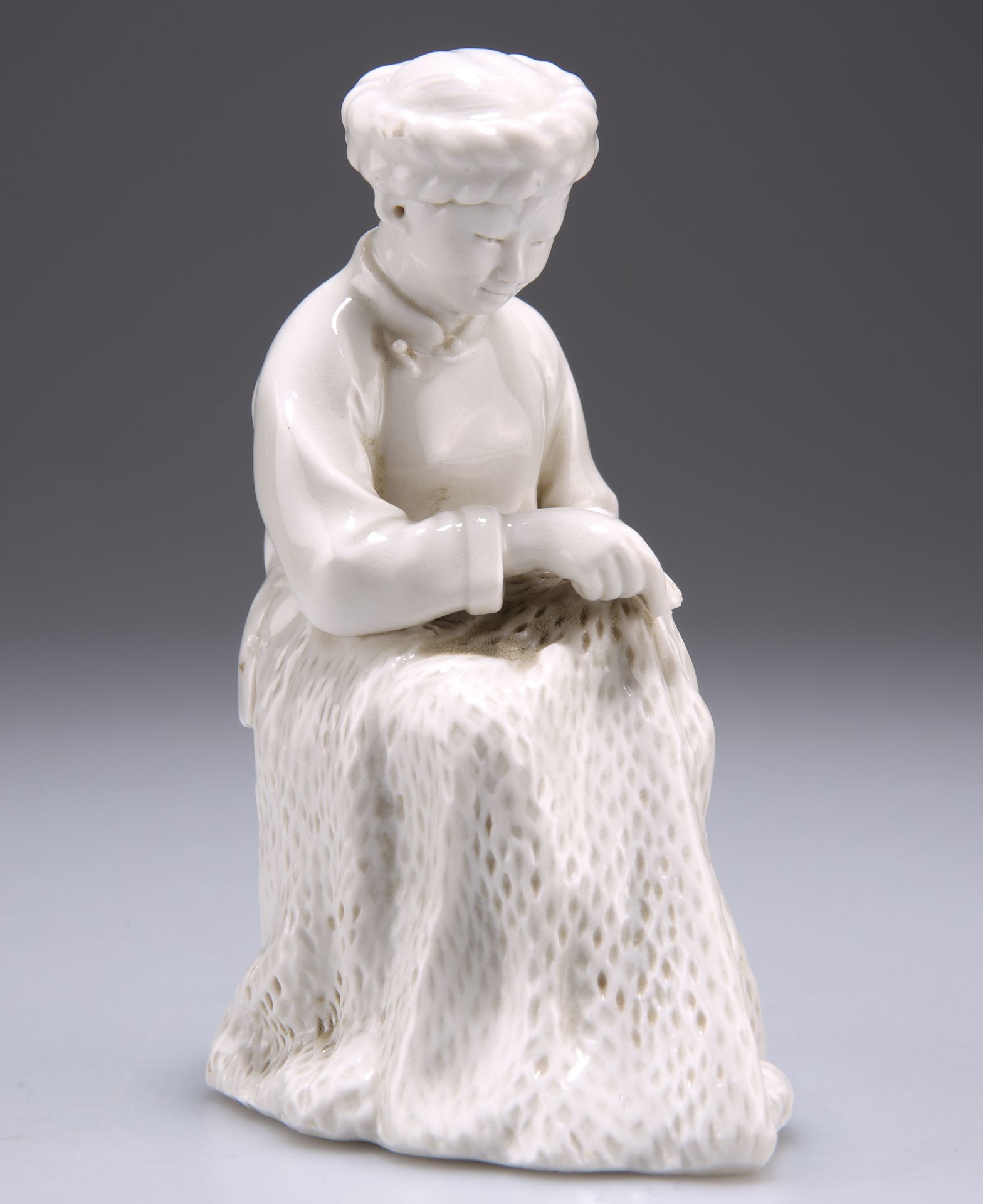 A BLANC DE CHINE FIGURE OF A SEATED WOMEN REPAIRING A FISHING NET