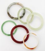 A GROUP OF FIVE JADE AND OTHER HARDSTONE BANGLES AND A GREEN GLASS BANGLE