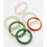 A GROUP OF FIVE JADE AND OTHER HARDSTONE BANGLES AND A GREEN GLASS BANGLE