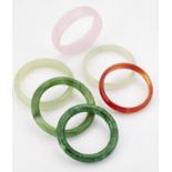A GROUP OF FIVE JADE AND OTHER HARDSTONE BANGLES AND A GREEN GLASS BANGLE