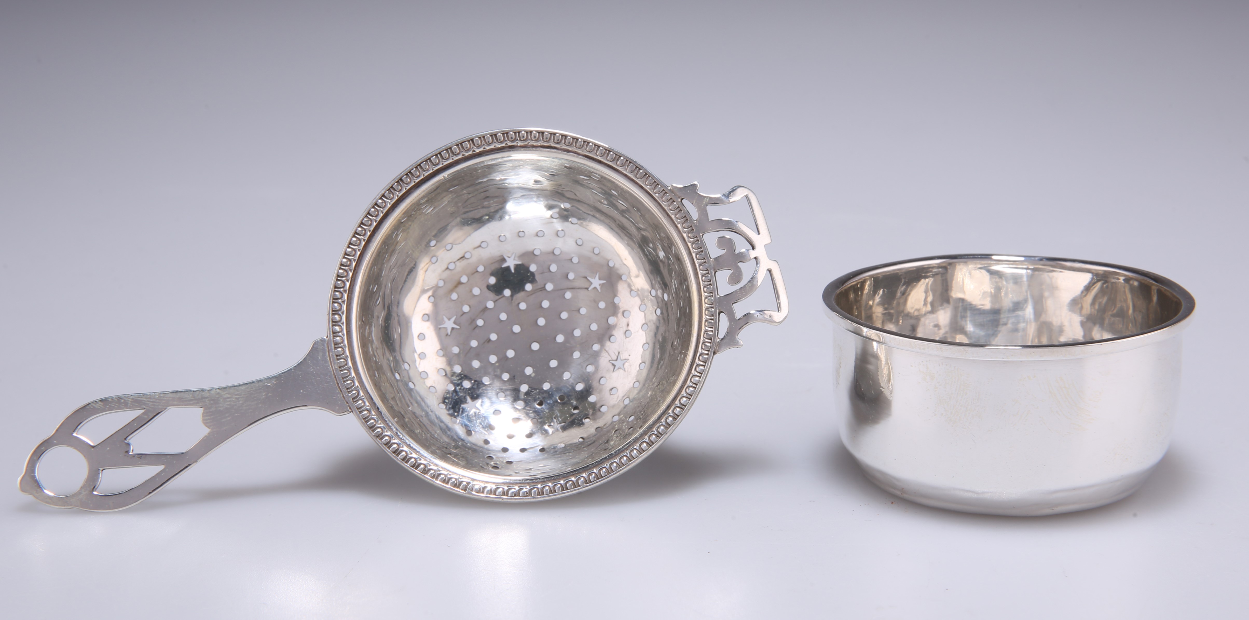 A GEORGE V SILVER TEA STRAINER ON STAND