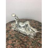 Art nouveau white metal figurine of a lady laying on a bed holding a tambourine aloft.