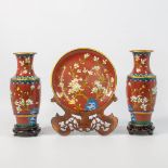 A pair of cloisonné vases and display plate on wood stands. Made of bronze and enamel.