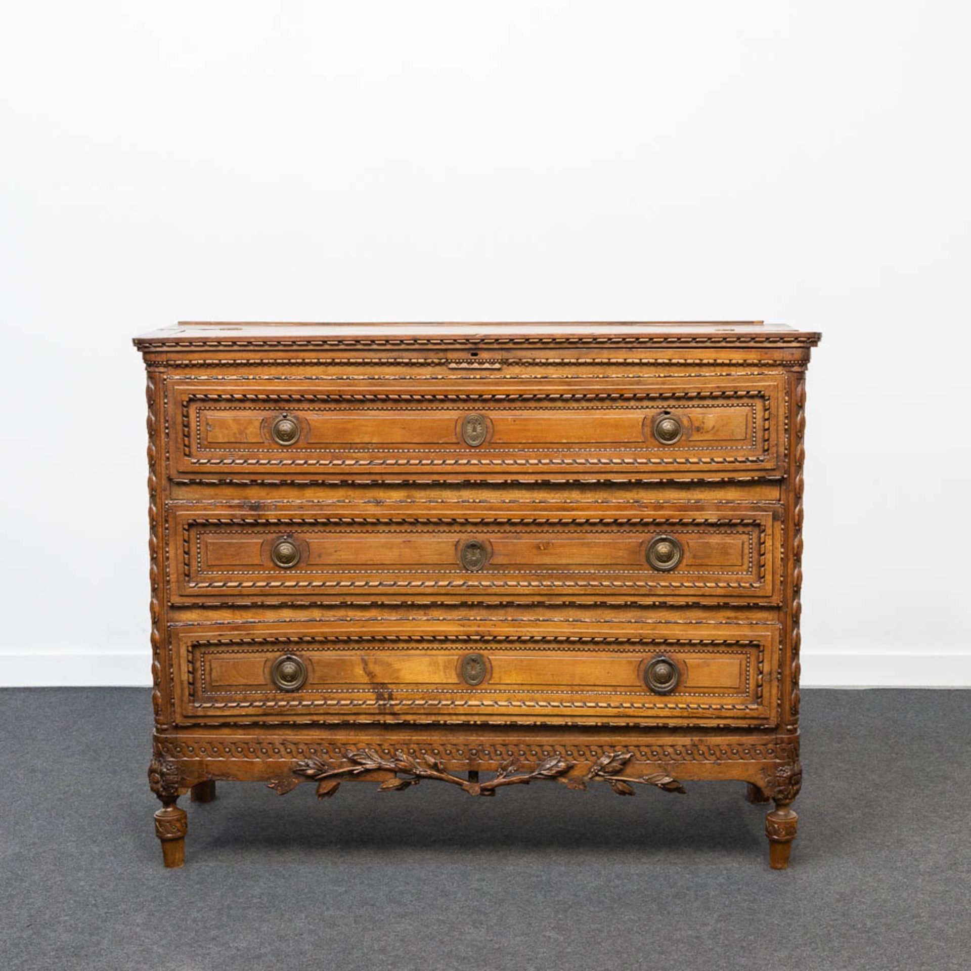 A wood sculptured commode in Louis XVI style, with 3 drawers and a hidden desk. 18th century.