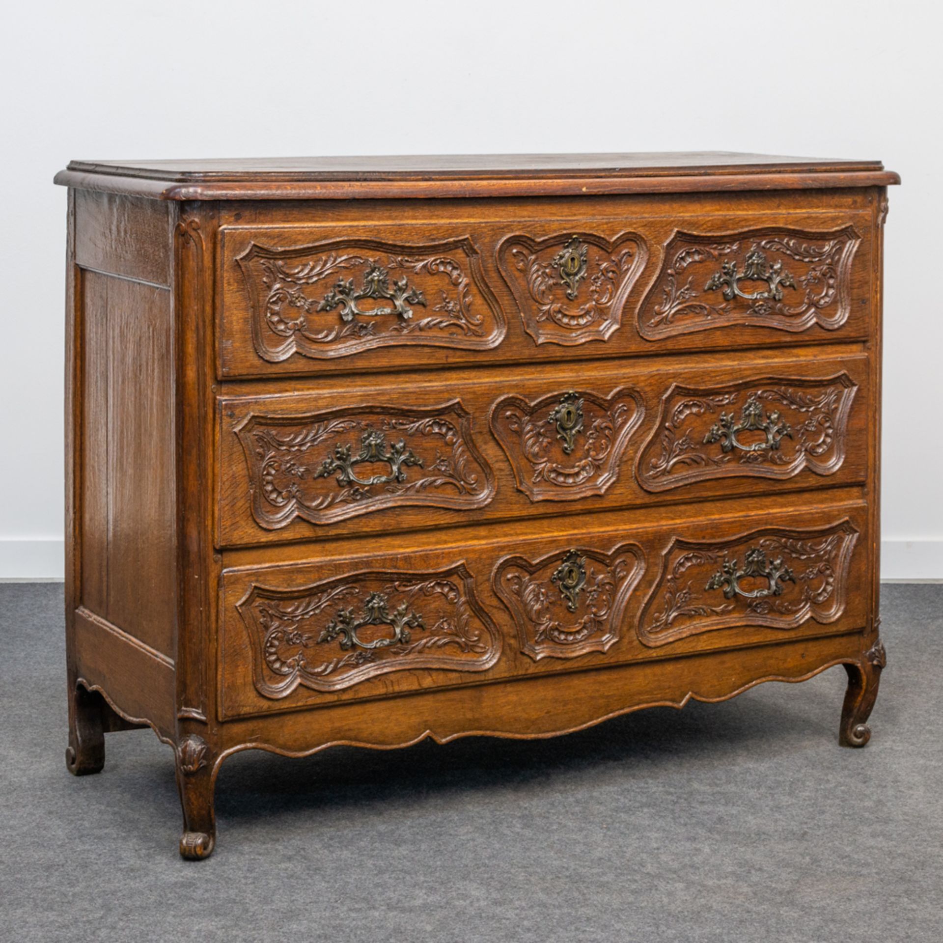 An antique commode with 3 drawers in the Louis XV period, sculptured decor, and mounted with bronze.