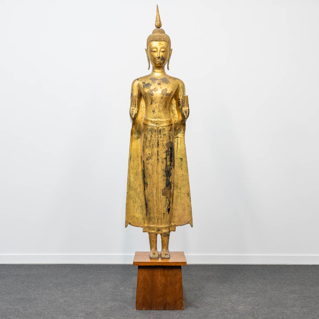 An antique buddha made of bronze and standing on a wood base. (28 x 48 x 180 cm)