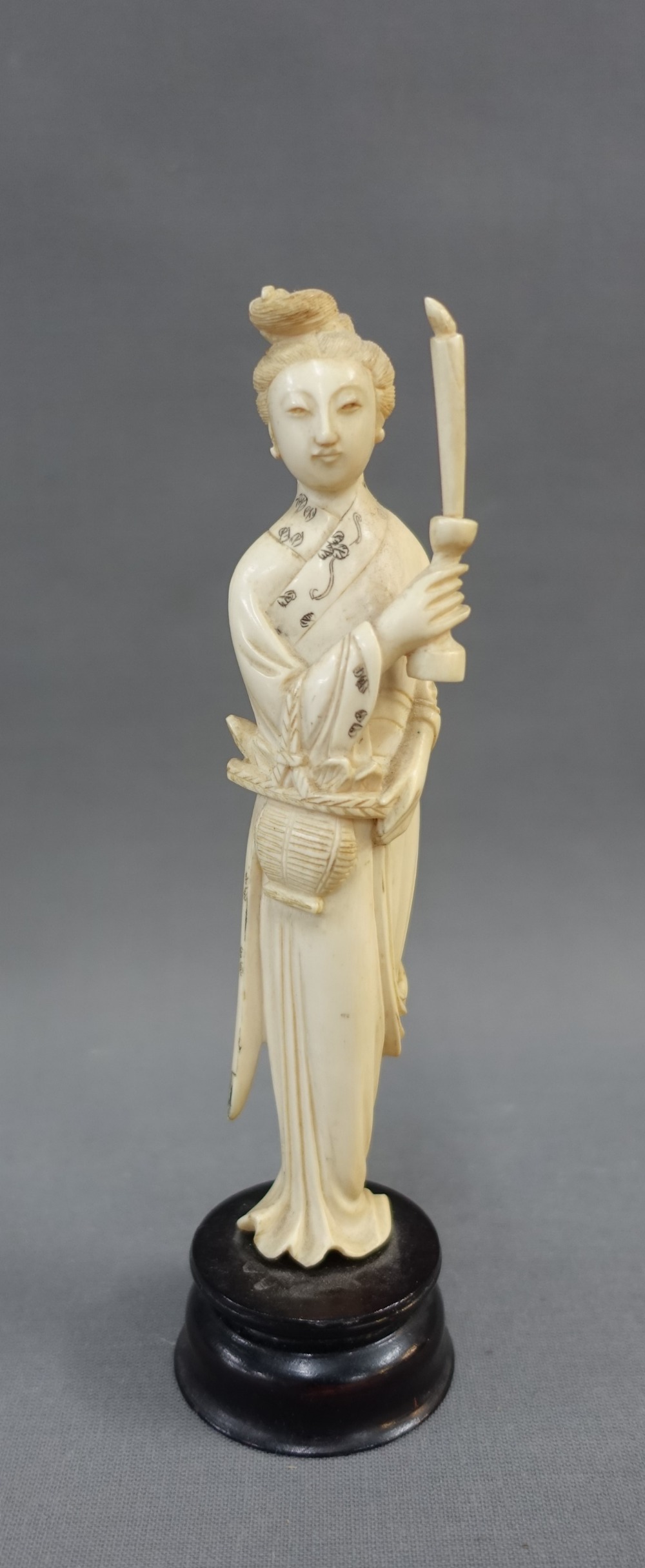 Early 20th century ivory okimono of a woman, modelled standing with a candle, on a wooden plinth