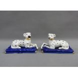 A pair of black and white hounds, on blue rectangular plinth bases, 13cm long (2)