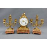 Gilt metal and pink hardstone clock garniture, the dial surmounted by birds, brass movement striking