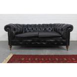 Black leather buttonback Chesterfield sofa on mahogany legs with brass caps and castors, 76 x 188cm