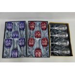 Two sets of six boxed crystal wine glasses, one set blue the other set red, together with a boxed