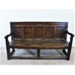 An antique dark oak bench with five panelled back, open arms with scrolling uprights, solid seat and