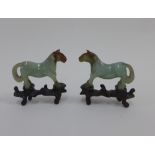 A pair of green jadeite horses with hardwood stand, (one with losses to the leg) 7cm high (2)