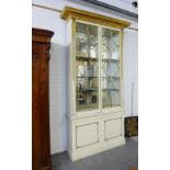 White painted cabinet of tall proportions, with an overhanging giltwood pelmet top over a pair of
