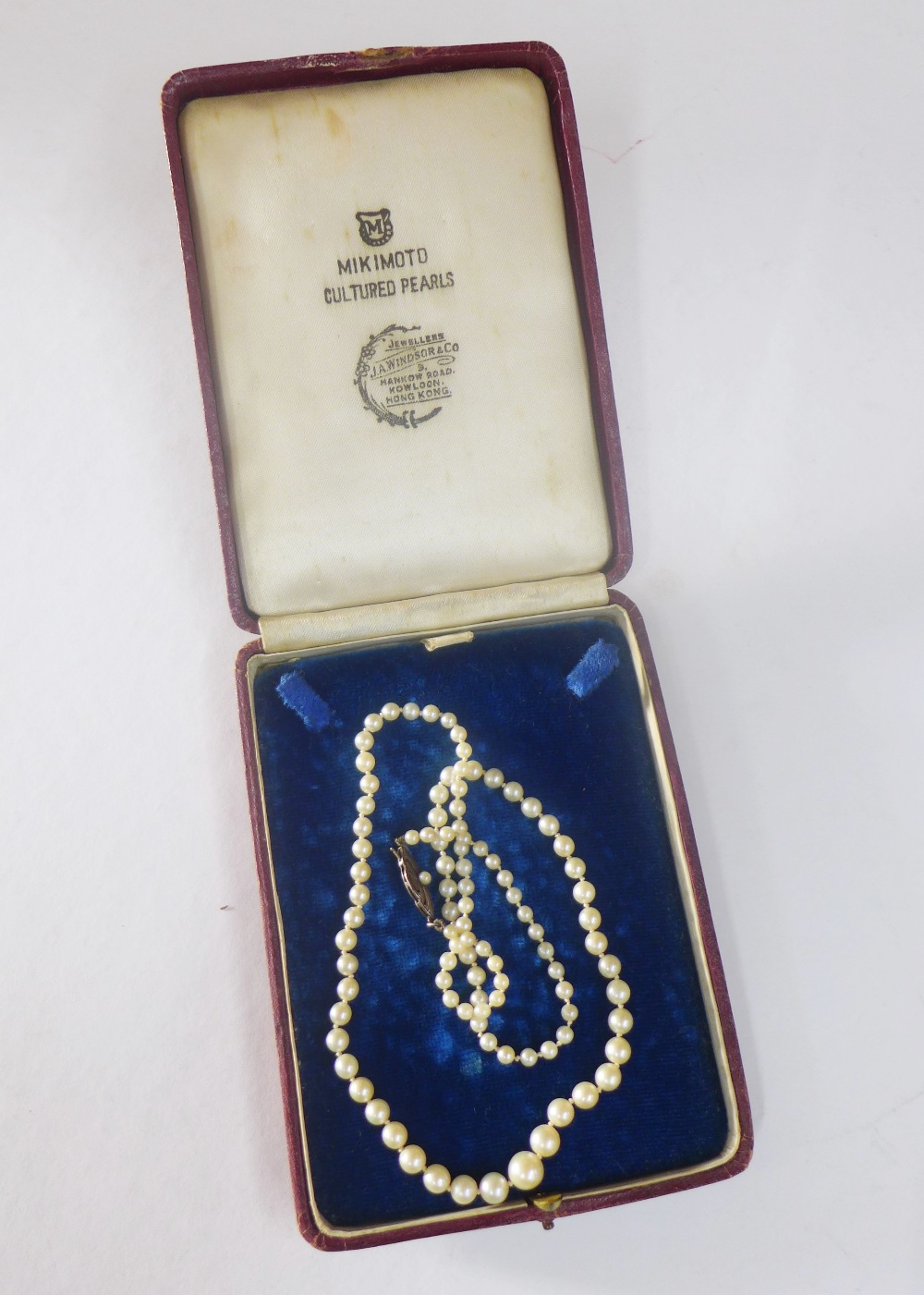 A strand of cultured pearls with a silver and seed pearl clasp, within a Mikimoto, Hong Kong box