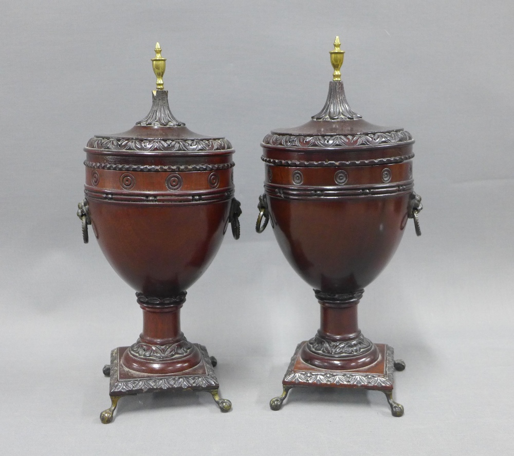 A pair of stained wooden urn vases with domed covers and brass finials, on brass claw and ball feet,