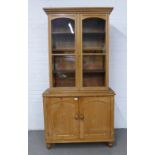 Pine two part cabinet, the top with glazed doors and shelved interior over a base with cupboard