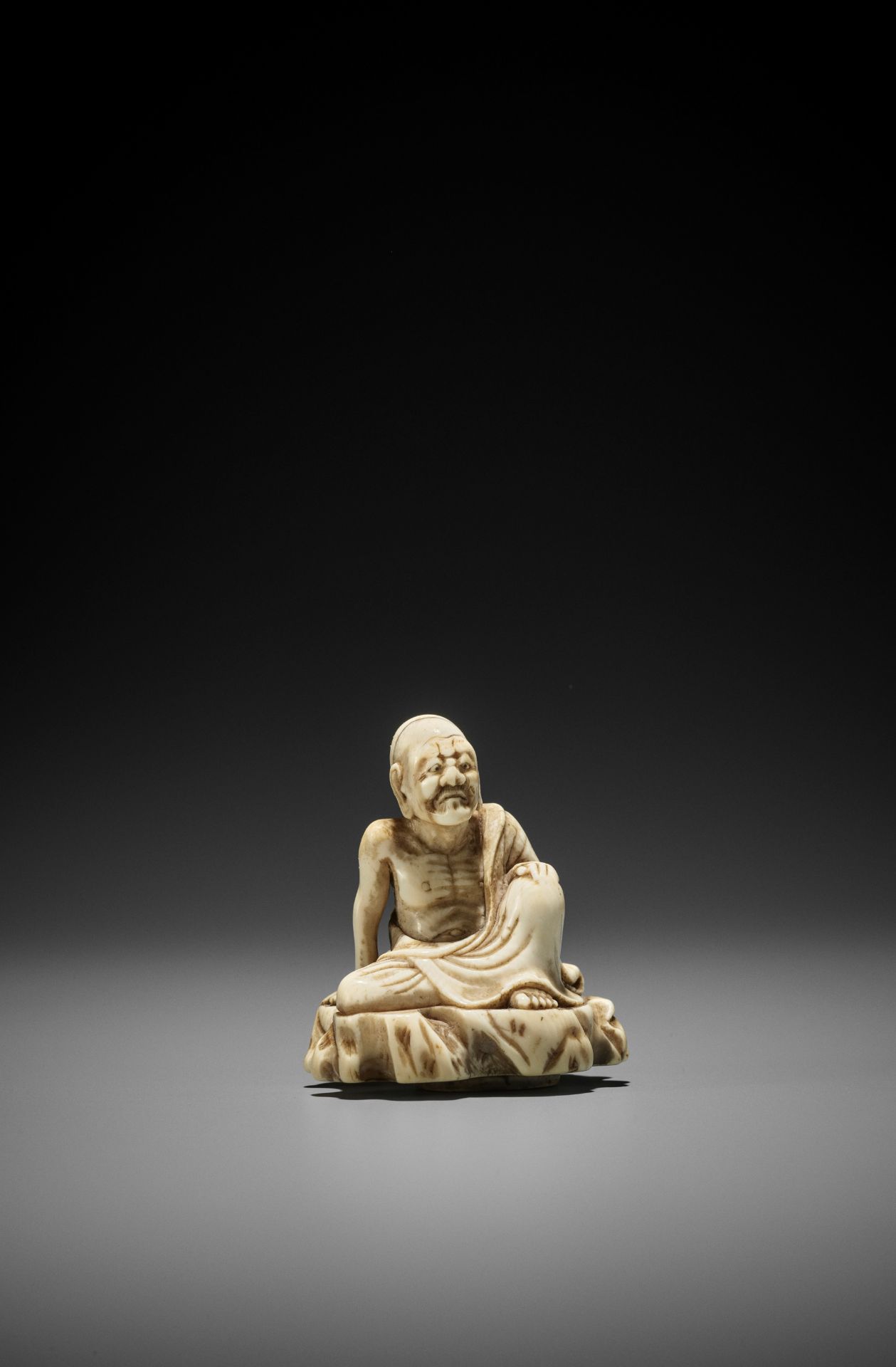 AN UNUSUAL AND EARLY TOBORI STYLE IVORY NETSUKE OF A RAKAN ON A ROCK