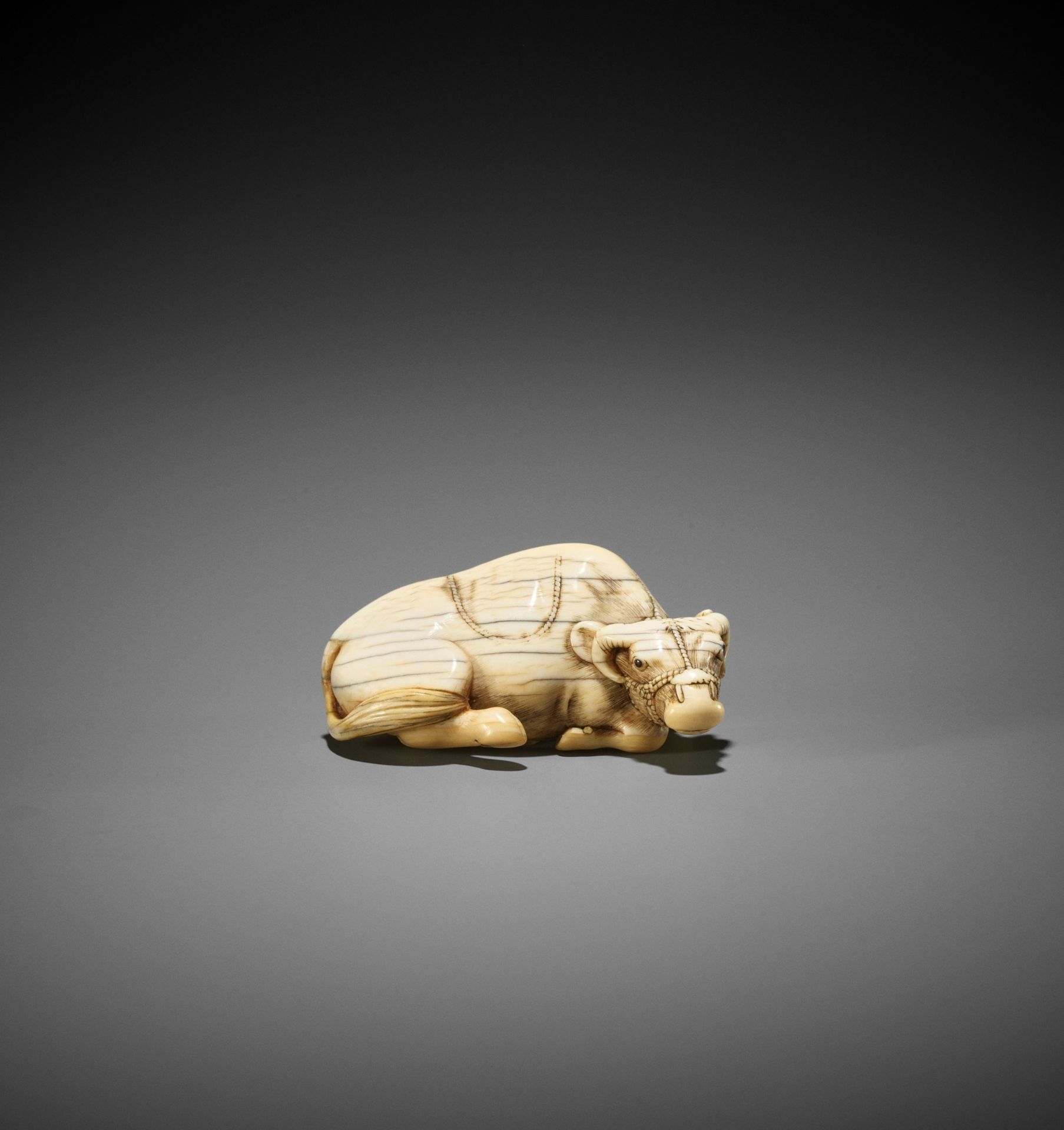 TOMOTADA: AN IVORY NETSUKE OF A RECUMBENT OX