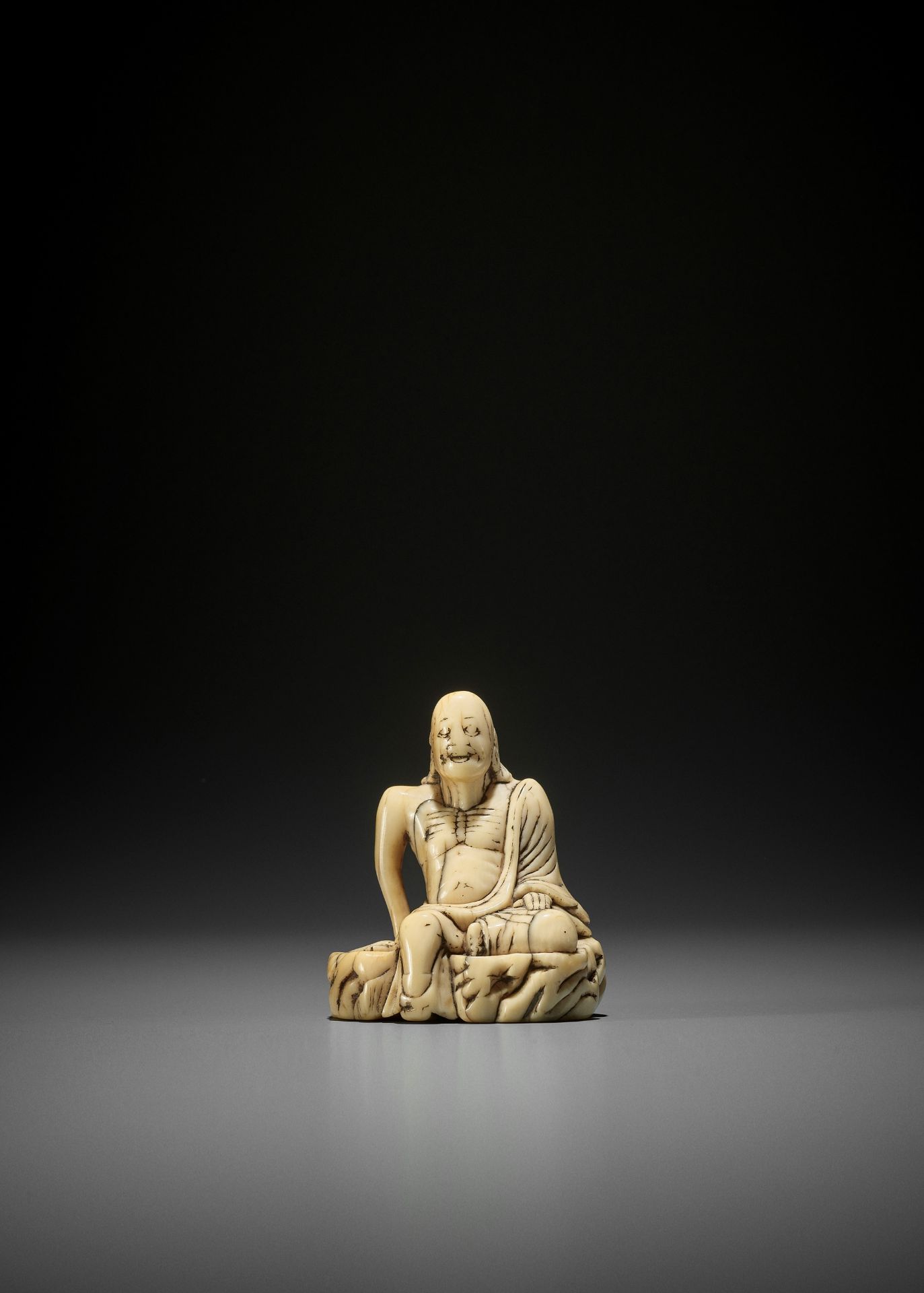 A LARGE AND EARLY IVORY TOBORI NETSUKE OF A RAKAN ON A ROCK